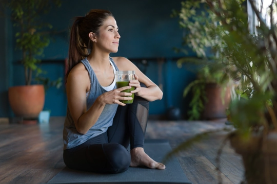 A woman sitting on a yoga mat with a smoothie.