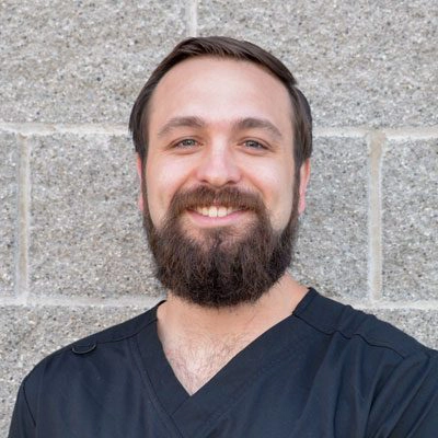 Dr. Dillan Friedrichs smiling in front of a stone wall.